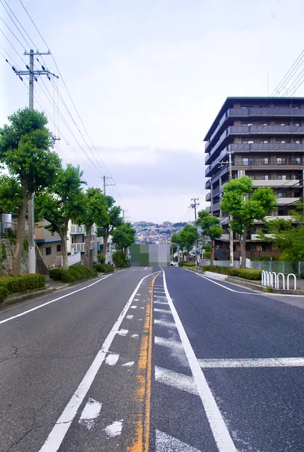 街路樹とマンションの並ぶ、遠くの街並みへ下る大通り