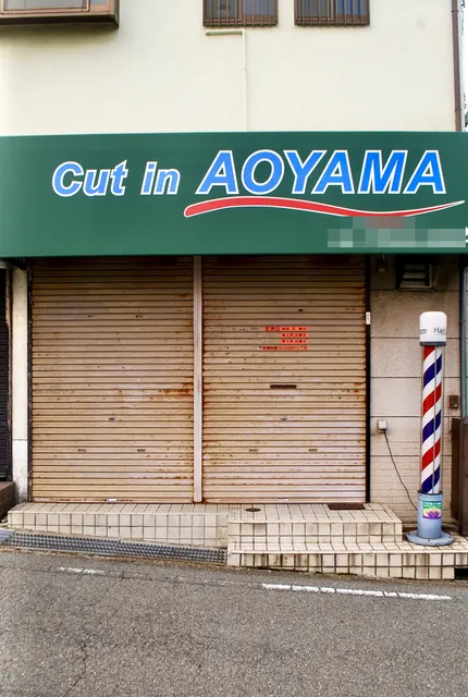 緑の看板とサインポールのある、シャッターの閉まった理容店