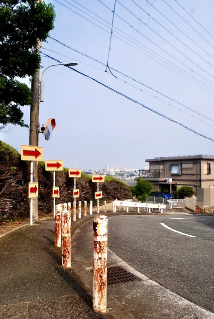 赤い矢印の標識とさびたポールが並ぶ、大きなカーブの道
