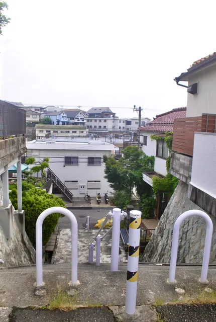 白い車止めの並ぶ階段の上から、坂の下の家並みを見下ろす風景