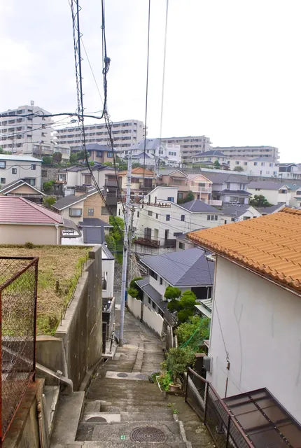 瓦屋根の家と擁壁のあいだを、下へ続く細い坂道