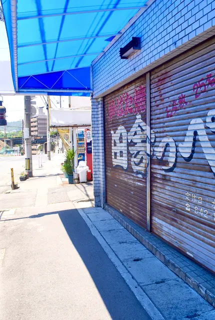 青いテントの下、絵の描かれたシャッターの店先と歩道