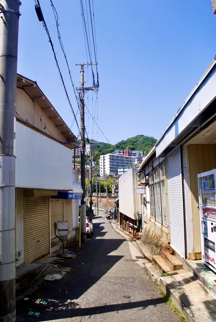 シャッターの店が並ぶ路地の先に、線路の土手が見える風景
