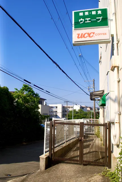 喫茶・軽食の看板が下がる建物と、茶色い門扉のある坂道