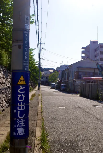 「とび出し注意」の看板の巻かれた電柱と、住宅街の坂道