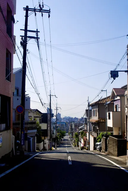 電柱と電線が並び、遠くの街並みへ下っていく坂道