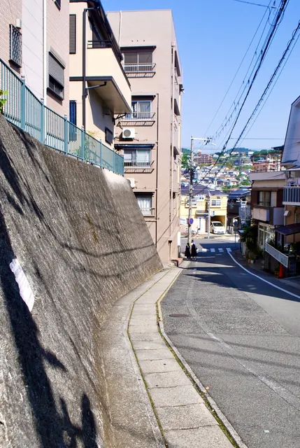 石垣に沿ってカーブする坂道の先に、遠くの街並みが見える風景
