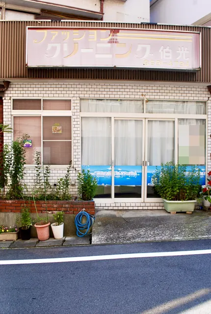 色あせたクリーニング店の看板と、植木鉢の並ぶ店先