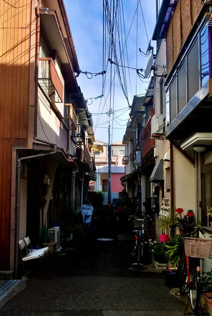 両側に家が迫る細い路地と、頭上で交差する電線