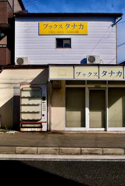 黄色い看板の建物と、古い自動販売機のある店先