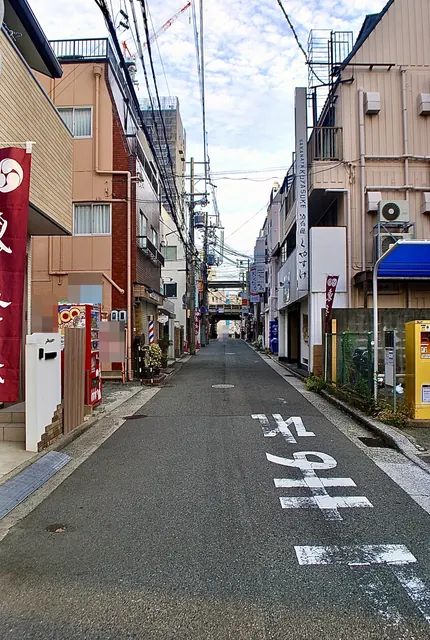 店の看板やのぼりが並び、奥に高架の見えるまっすぐな通り