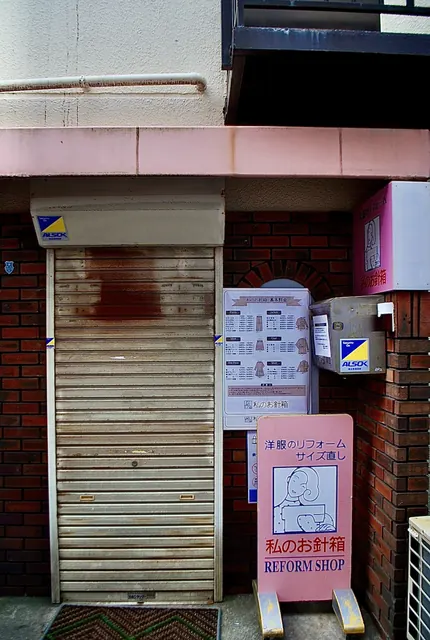 レンガの壁にシャッターと立て看板のある、小さな洋服直しの店