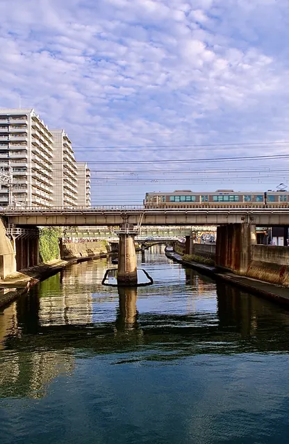 青空の下、川の河口に架かる鉄橋を電車が渡る風景