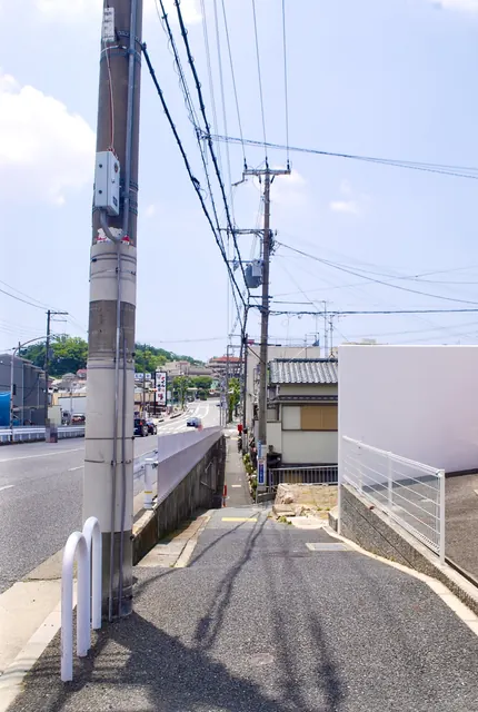 大きな電柱の脇から、電線の下を奥へ続く歩道と大通り