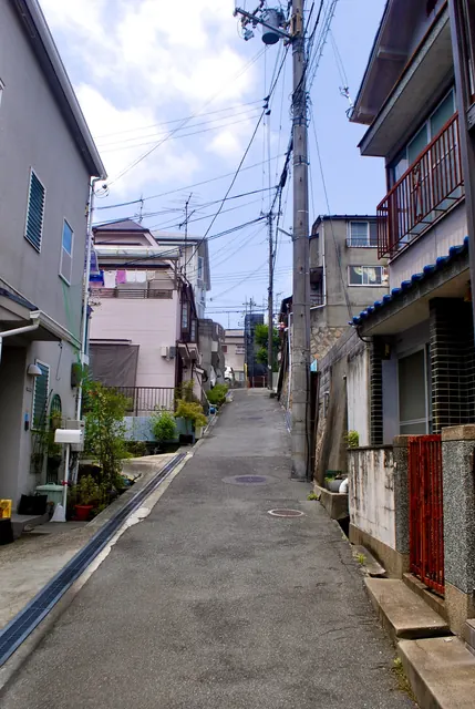 電線が空を横切る中、住宅のあいだを上っていく坂道