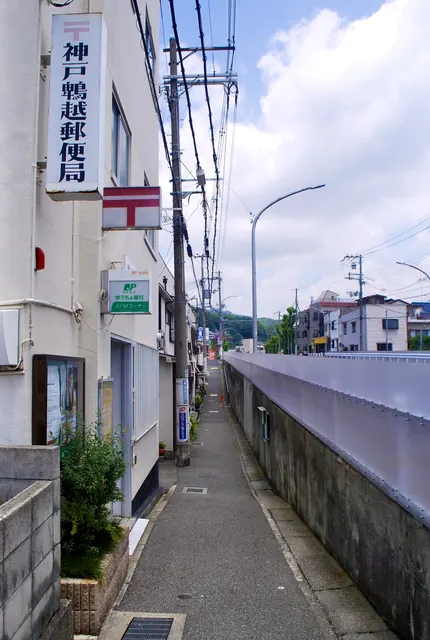 縦長の郵便局の看板と、高い壁に沿ってまっすぐ続く細い歩道