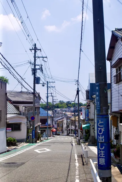 幾重にも張られた電線の下、町並みへ下っていく広い坂道