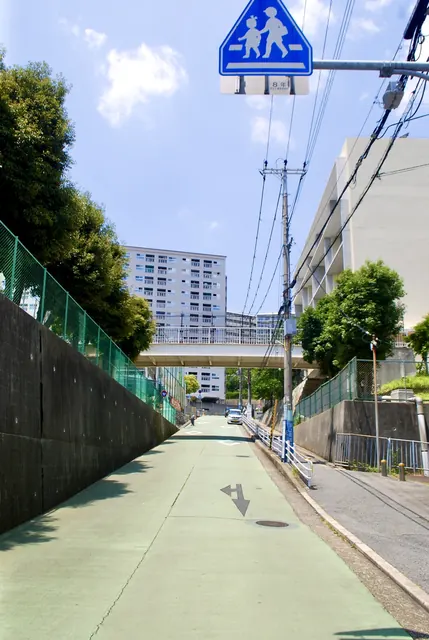 横断歩道の標識の下、歩道橋と団地へ向かう緑色の坂道