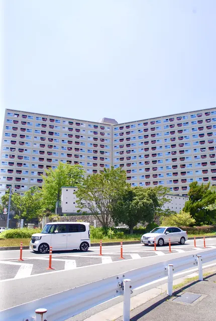 青空の下、木々の奥に横へ長く広がる大きな団地