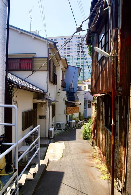 さびたトタン壁と家々のあいだの路地の奥に、団地が見える風景