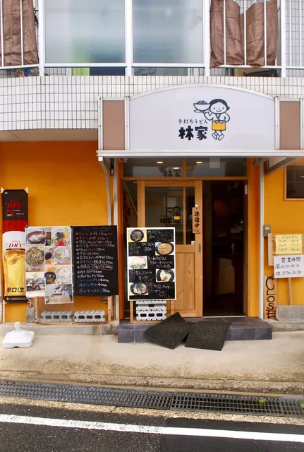 オレンジの壁に、メニューの黒板と写真が並ぶうどん店の店先