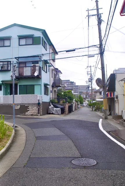白い格子の塀の家の前を、カーブしながら続く住宅街の道