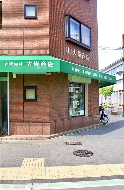 緑の日よけに「有限会社 大條商店」と書かれた、レンガの建物の角