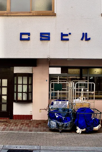 青い文字の「CSビル」の看板と、台車の並ぶ古いビルの入口