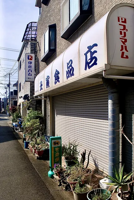 「伊藤ハム」「プリマハム」の看板と、植木鉢の並ぶ食品店