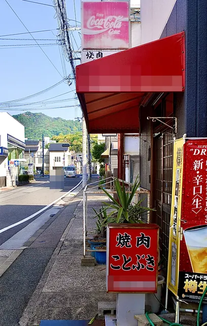 「焼肉 ことぶき」の立て看板と、山並みの見える通り