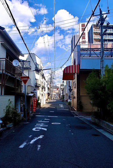 雲の浮かぶ青空に電線が幾重にも張られた、人通りの少ない通り