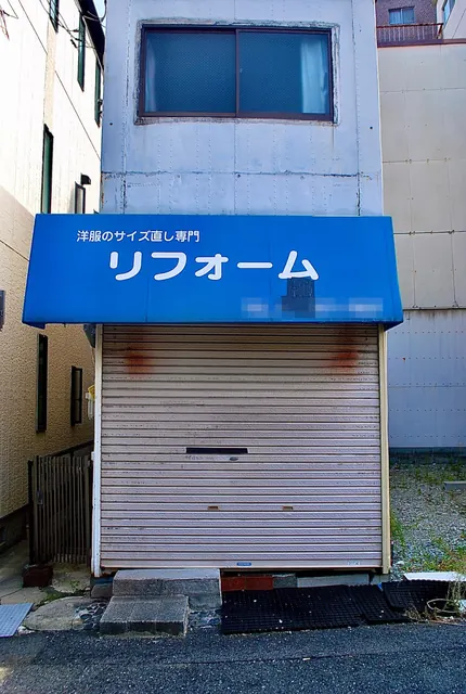 青い日よけの下に、閉まったシャッターのある細長い建物