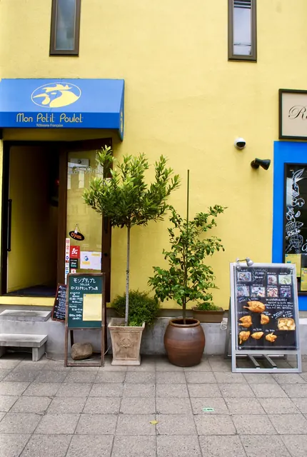 黄色い壁に青い日よけ、植木の並ぶロースト チキンの店先