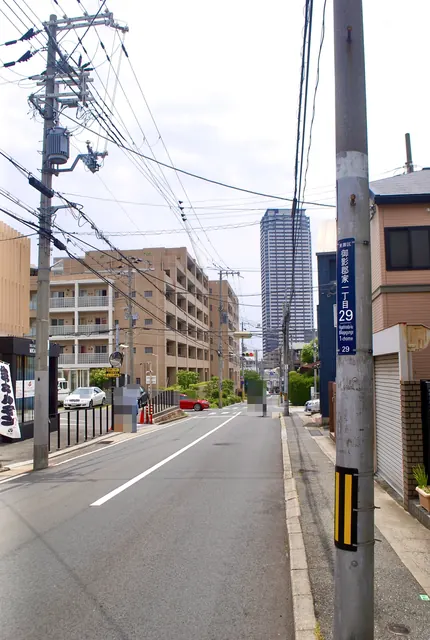 町名表示のある電柱の脇から、高層マンションの見える通り