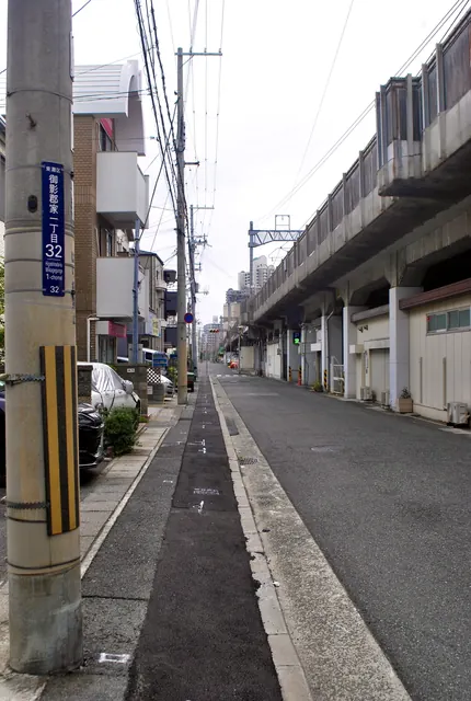 町名表示のある電柱の脇から、高架沿いにまっすぐ続く通り