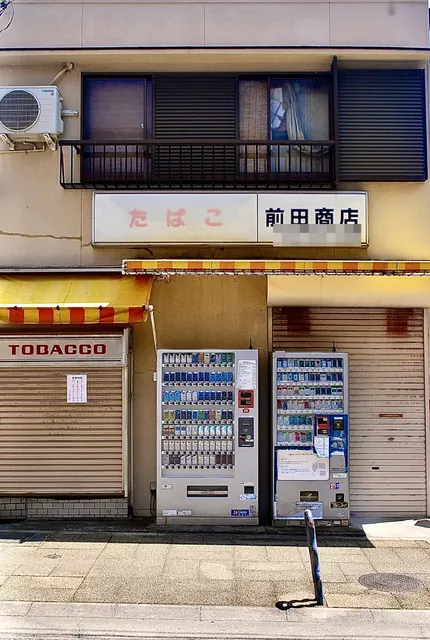 しましまの日よけとたばこの自動販売機が並ぶ、たばこ屋の店先