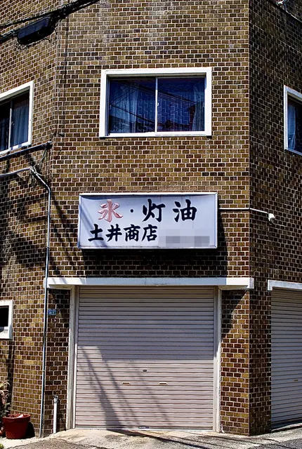 茶色いタイルの角の建物に、「氷・灯油」の看板が残る商店