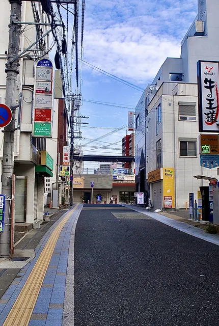 縦長の看板と電線が並び、奥へ続く駅前の通り