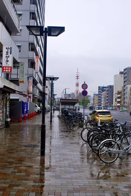 店の看板が並び、雨に濡れたタイルの歩道が続く大通り