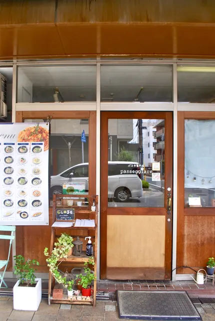 木の扉と窓辺にメニューと植木の並ぶ、パスタ専門店の入口