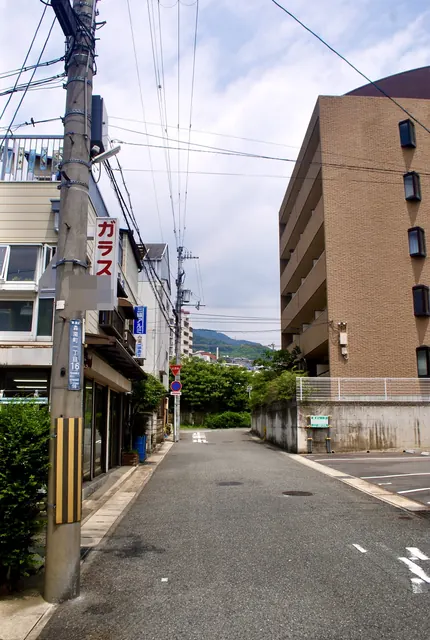 「ガラス」の看板と町名表示の電柱の先に、緑と山が見える道