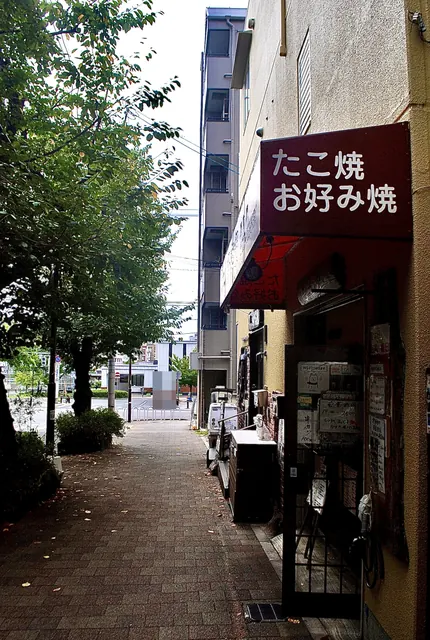 「たこ焼 お好み焼」の看板と、並木の続く歩道