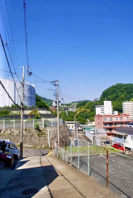 電線の張られた坂道の先に、山と町並みが広がる風景