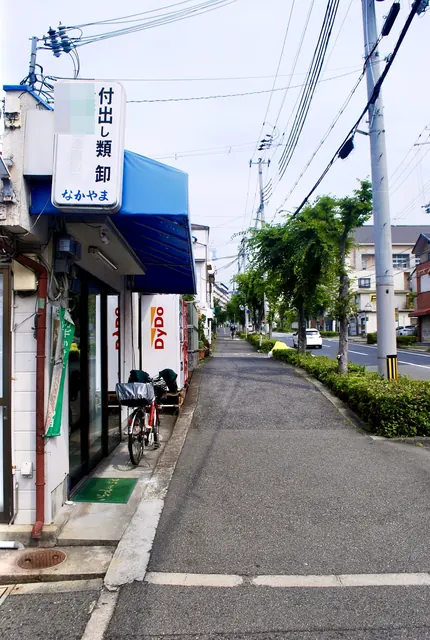「付出し類卸」の縦看板と自動販売機が並ぶ、並木沿いの歩道