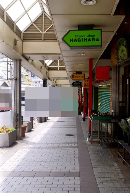 花屋の看板と鉢植えが並ぶ、屋根つきの商店街の歩道