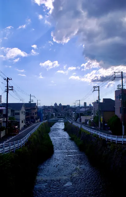 雲の広がる空の下、石積みの川がまっすぐ街並みへと続く風景