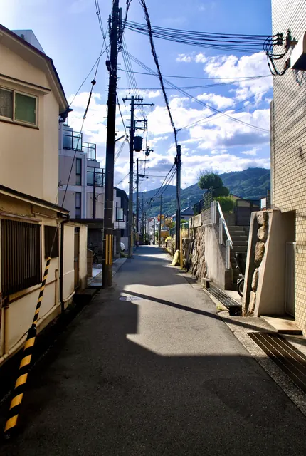 石垣と電柱の並ぶ細い道の先に、六甲の山並みが見える風景