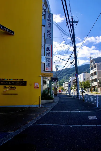 黄色い壁の建物と縦長の看板の先に、山へ向かって続く道