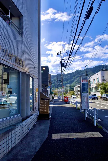 赤い郵便ポストとバス停の立つ歩道の先に、山並みが見える風景