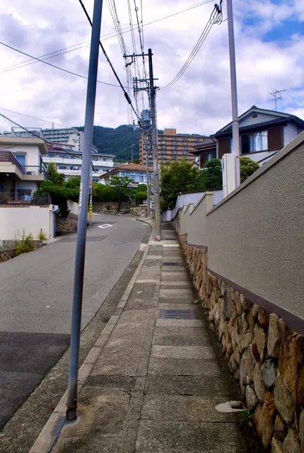石垣に沿って上っていく歩道と、奥に見える山とマンション